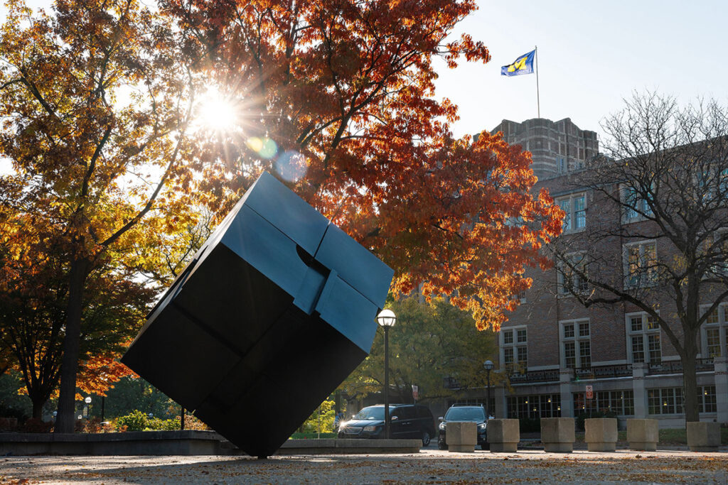 Sunlight filters through trees with red and orange leaves and casts a flare onto the Cube in Regents Plaza on a crisp fall morning.