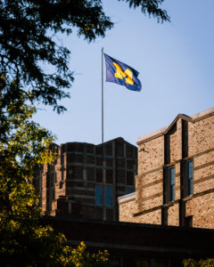 The Michigan Union flag waves against a clear blue sky during sunrise.