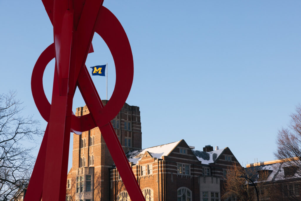 The Michigan Union's Block M flag seen through the sculpture Orion on a winter day